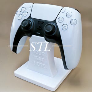 Może przedstawiać: Biało-czarny kontroler do gier na białym stojaku. Kontroler ma czarne joysticki i przyciski z symbolami. Stojak ma napis "STL YOUR TEXT HERE".