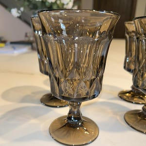 Può includere: Set di sei calici da acqua colorati di marrone. Ogni bicchiere presenta un motivo verticale strutturato e un motivo a diamante vicino alla base. I calici hanno una base rotonda e sono disposti su una superficie bianca.