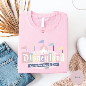 a pink t-shirt with a Disneyland logo, a pair of blue jeans, and some decorative elements such as a palm leaf and a beige sweater.