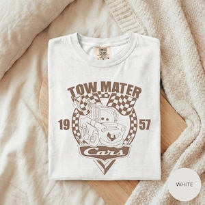 A white t-shirt with a graphic design featuring a tow truck and the text "TOW MATTER Cars" printed on it.