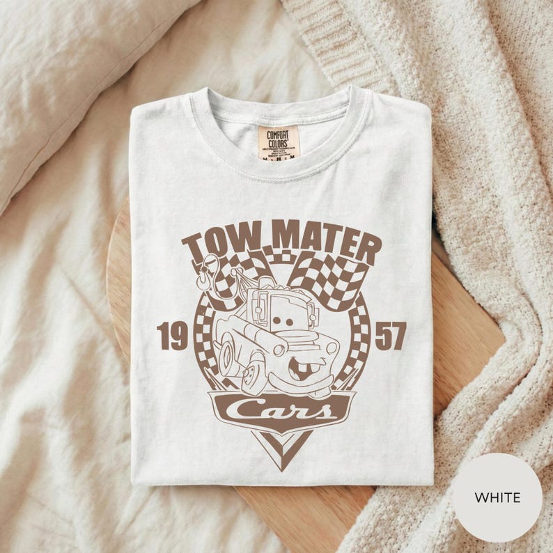A white t-shirt with a graphic design featuring a tow truck and the text "TOW MATTER Cars" printed on it.