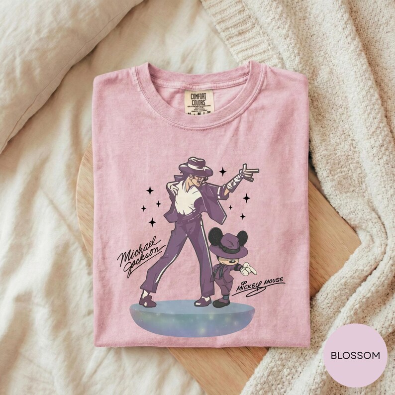 A pink t-shirt with a graphic design featuring a man and a character, likely Mickey Mouse, along with the text "Michael Jackson" and "Mickey Mouse".
