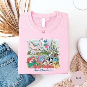 A pink t-shirt with a Disney-themed graphic, including characters like Dumbo, Minnie Mouse, and Mickey Mouse, along with a castle and other Disney-related imagery.