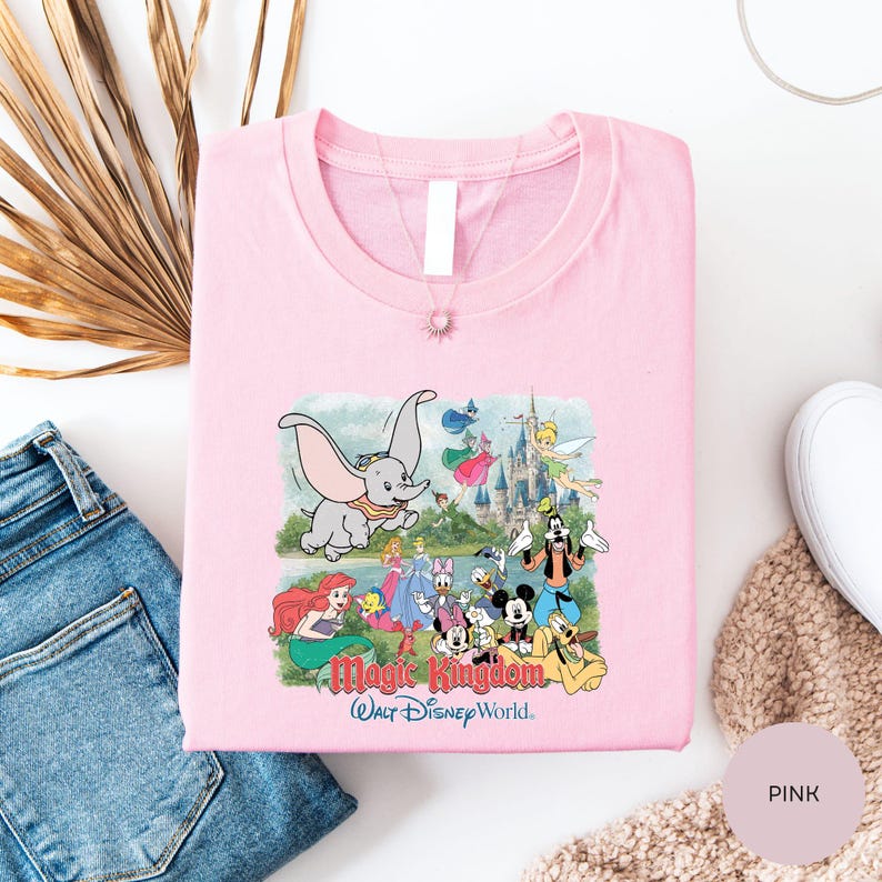 A pink t-shirt with a Disney-themed graphic, including characters like Dumbo, Minnie Mouse, and Mickey Mouse, along with a castle and other Disney-related imagery.