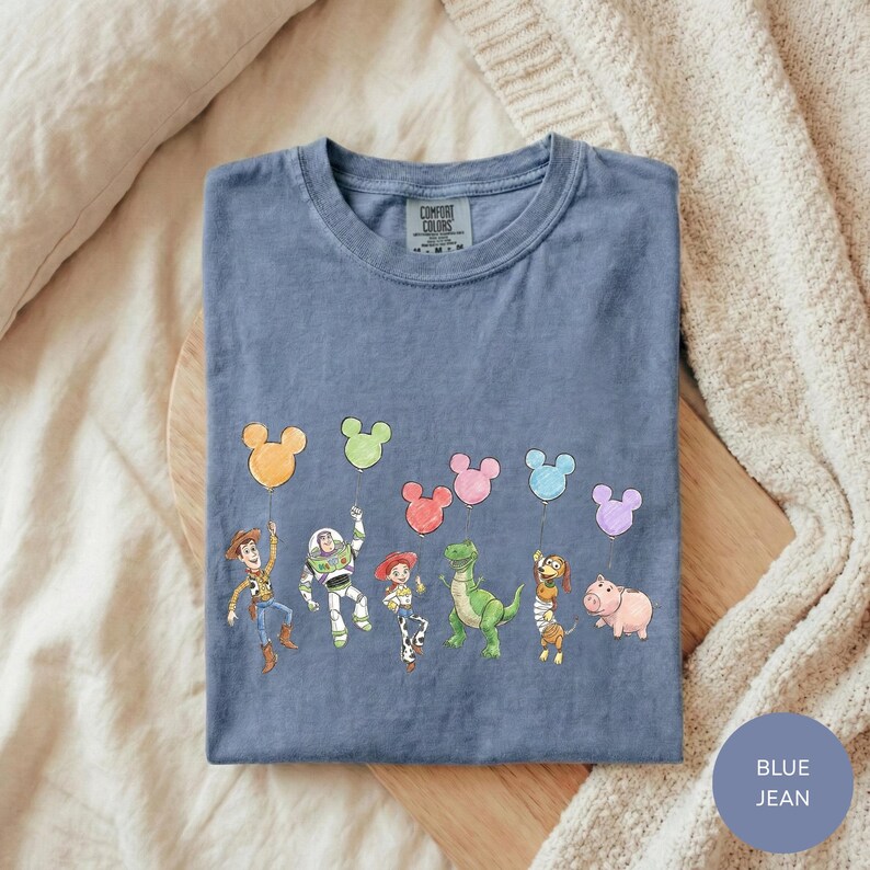 A blue t-shirt with a graphic design featuring characters from the Toy Story movie, including Woody, Buzz Lightyear, and other beloved characters.