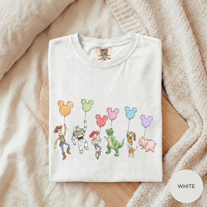 A white t-shirt with a graphic design featuring characters from the Toy Story movie, including Woody, Buzz Lightyear, and other beloved characters.