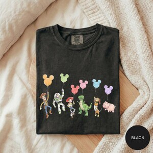 A black t-shirt with a graphic design featuring characters from the Toy Story movie, including Woody, Buzz Lightyear, and other beloved characters.