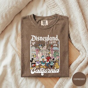 A t-shirt with a Disney-themed graphic design, featuring characters from the Disney theme park, including Mickey Mouse, Donald Duck, and Goofy.