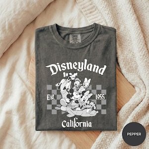 A gray t-shirt with a graphic design featuring Disney characters and text, laid out on a wooden surface.