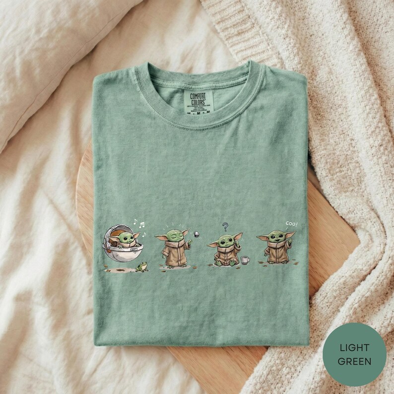 A green t-shirt with a graphic design depicting three baby alien characters from the Star Wars series, along with the text "Cool!"