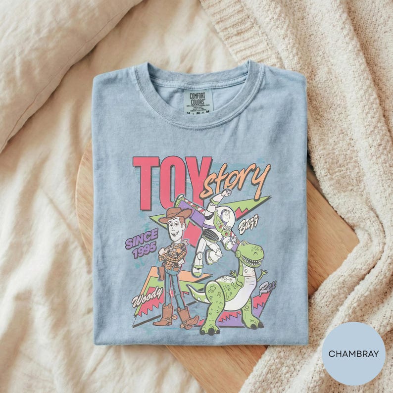 A t-shirt with a colorful graphic design featuring characters from the Toy Story movie, including Woody and Buzz Lightyear, along with the text "TOY STORY SINCE 1955" and "Woody".
