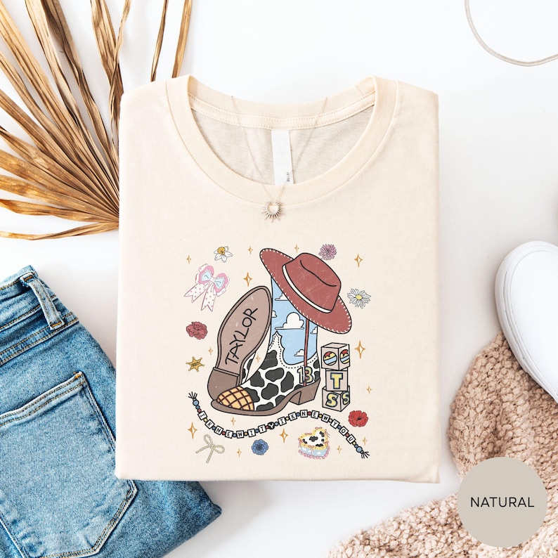 a white t-shirt with a cartoon character and various decorative elements, such as a cowboy hat, flowers, and stars, laid out on a white background.