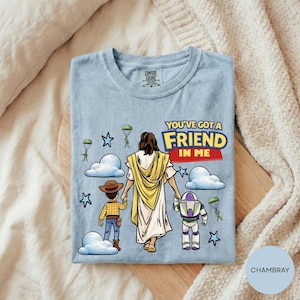 A t-shirt with a cartoon illustration of a person holding hands with a boy and a robot, along with the text "You've got a friend in me" and various other characters and objects.