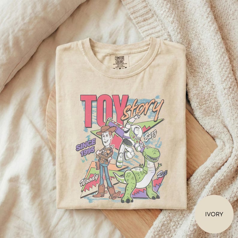 A beige t-shirt with a colorful graphic design featuring characters from the Toy Story movie, including Woody and Buzz Lightyear.