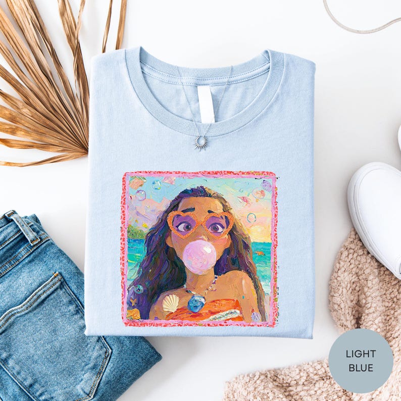 a light blue t-shirt with a colorful graphic of a young girl blowing a bubble gum bubble, surrounded by various clothing items and accessories.