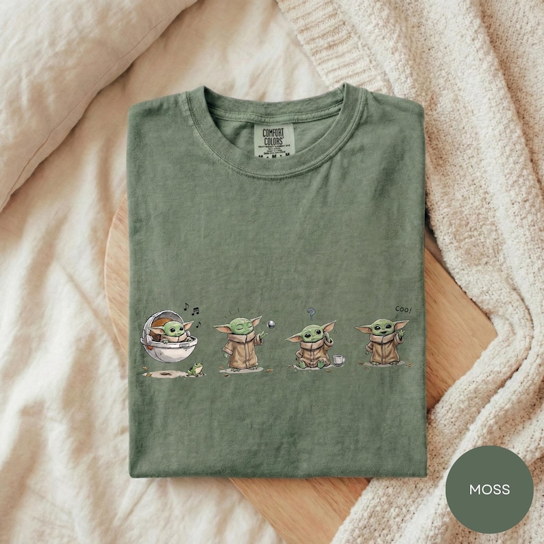 A green t-shirt with a graphic design depicting four baby alien characters from the Star Wars series, each in a different pose.