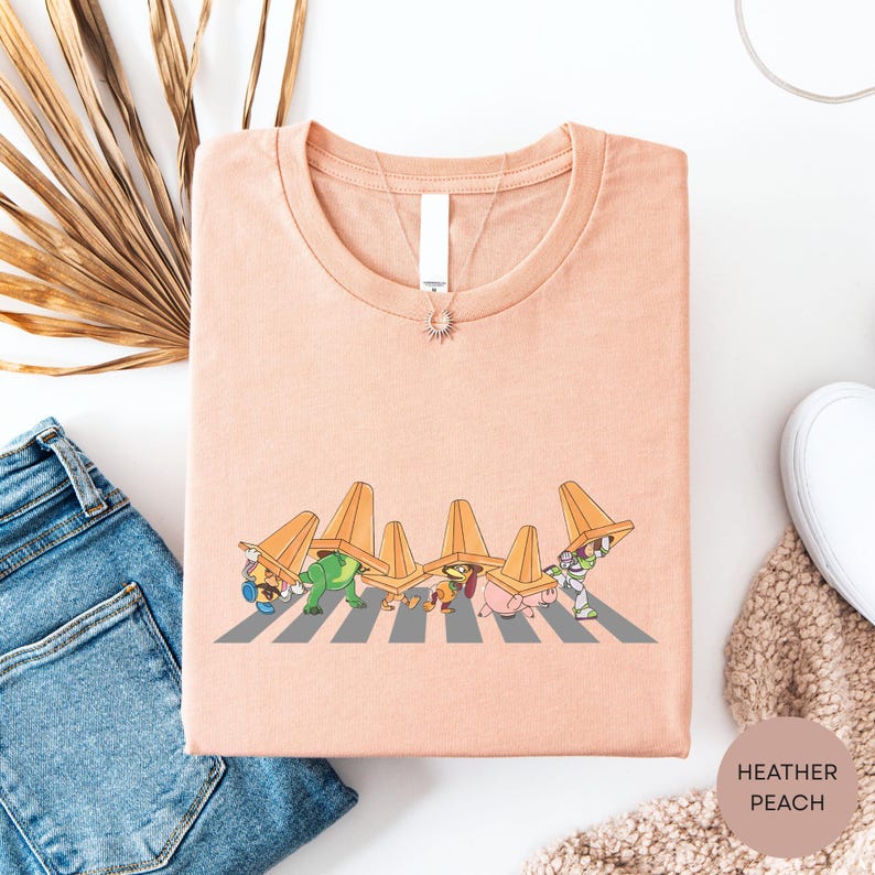 a pink t-shirt with a cartoon illustration of a group of cartoon characters wearing orange hats, along with a pair of blue jeans and a white scarf.