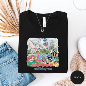 A black t-shirt with a Disney-themed graphic design, including characters from the Disney animated films, is displayed alongside a pair of jeans and a necklace.