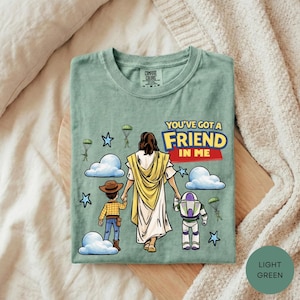 A green t-shirt with a cartoon illustration of a person holding hands with a child and a dog, along with a message that says "You've got a friend in me".