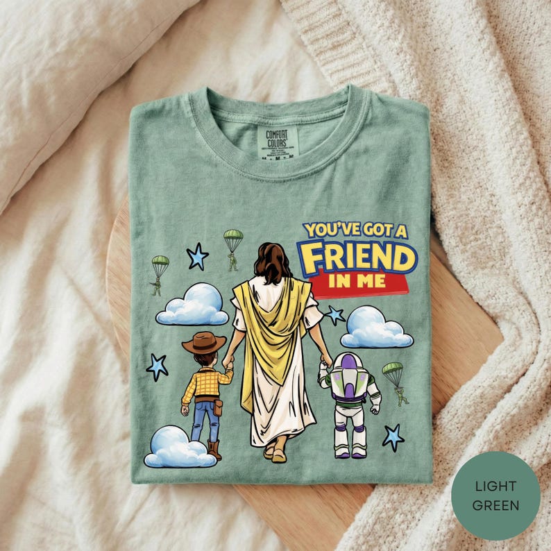 A green t-shirt with a cartoon illustration of a person holding hands with a child and a dog, along with a message that says "You've got a friend in me".
