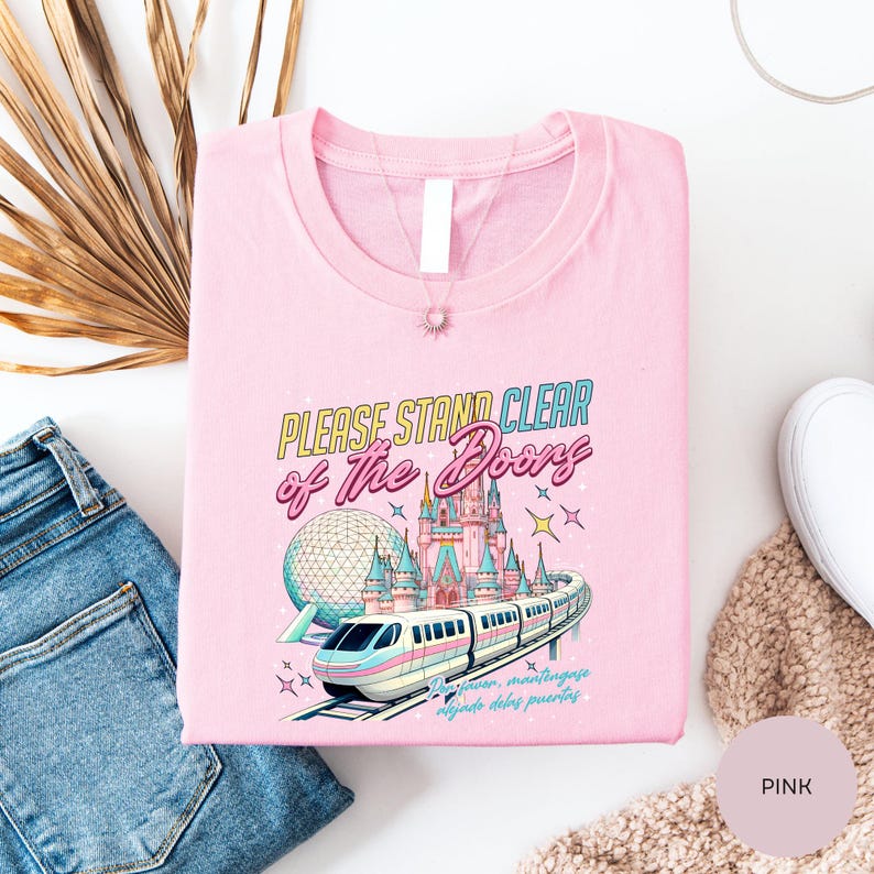 a pink t-shirt with a colorful graphic design depicting a train and a castle, along with the text "Please stand clear of the doors".