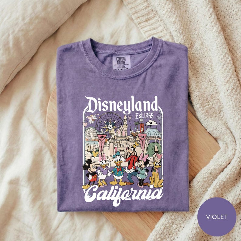 A purple t-shirt with a graphic design of Disney characters and the text "Disneyland Est. 1955 California" printed on it.