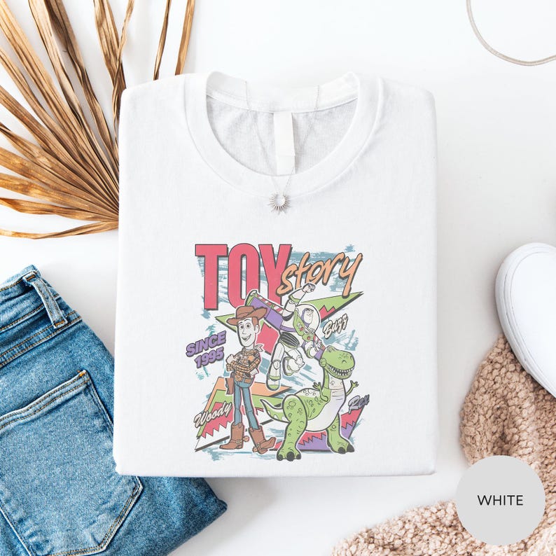 a white t-shirt with a colorful graphic of a character from the Toy Story movie, along with a denim shirt and some other clothing items.