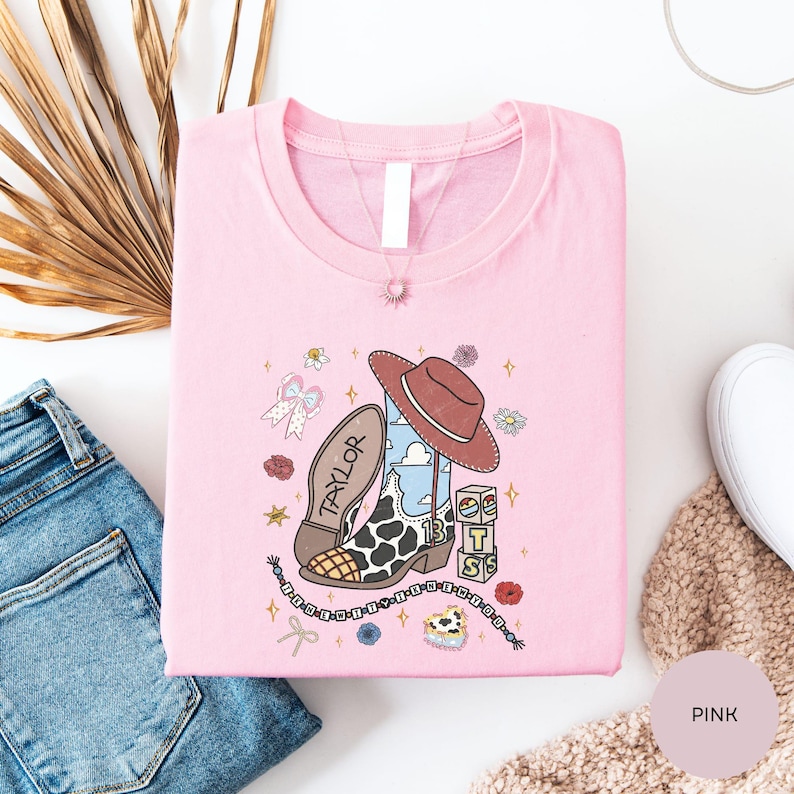 a pink t-shirt with a cartoon character and various accessories, such as a cowboy hat, a chain, and a flower, all set against a white background.
