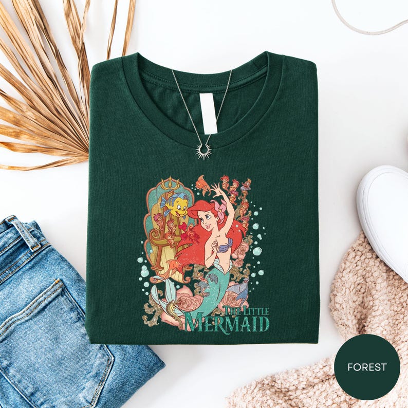 a green t-shirt with a colorful graphic of a mermaid character, along with a necklace and some other clothing items.