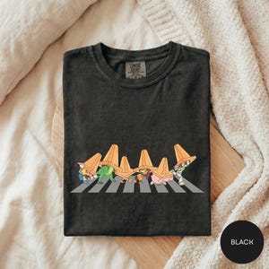 A black t-shirt with a graphic design depicting a group of cartoon characters crossing a road.