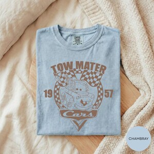 A light blue t-shirt with a graphic design featuring a tow truck and the text "TOW MATER Cars" printed on it.