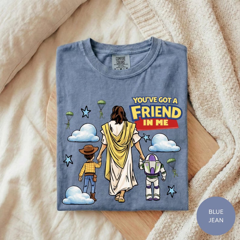 A blue t-shirt with a graphic design depicting a person in a yellow robe and a child, along with a Bible verse and a character from the Toy Story franchise.