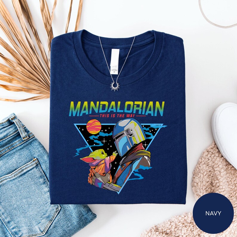 a navy blue t-shirt with a colorful graphic design depicting a character from the Star Wars series, specifically Mandalorian, in a space-themed setting.
