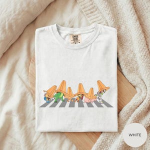 A white t-shirt with a graphic design depicting a group of cartoon characters crossing a road.