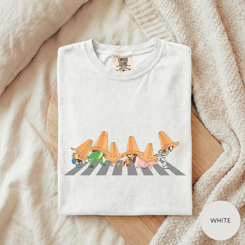 A white t-shirt with a graphic design depicting a group of cartoon characters crossing a road.