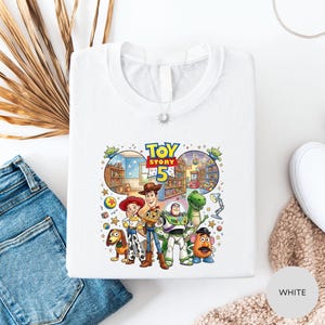 a white t-shirt with a colorful graphic of characters from the Toy Story movie, including Woody, Buzz Lightyear, and other beloved characters.