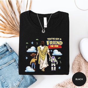 A black t-shirt with a graphic design depicting a person holding hands with two children, one of whom is wearing a cowboy hat. The text on the t-shirt reads "You've got a friend in me".