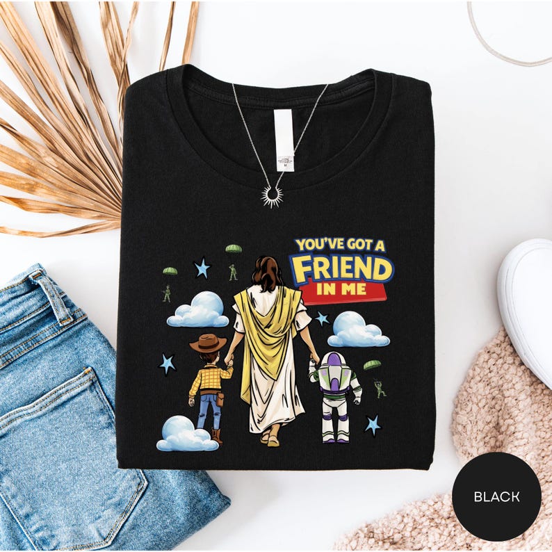 A black t-shirt with a graphic design depicting a person holding hands with two children, one of whom is wearing a cowboy hat. The text on the t-shirt reads "You've got a friend in me".
