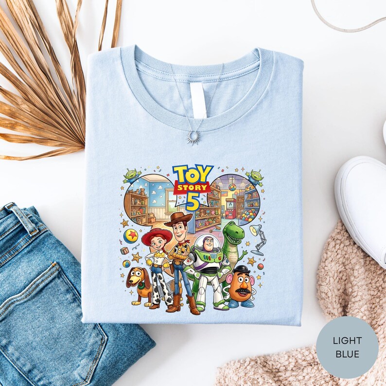 a light blue t-shirt with a colorful graphic of characters from the Toy Story movie, including Woody, Buzz Lightyear, and other beloved characters.