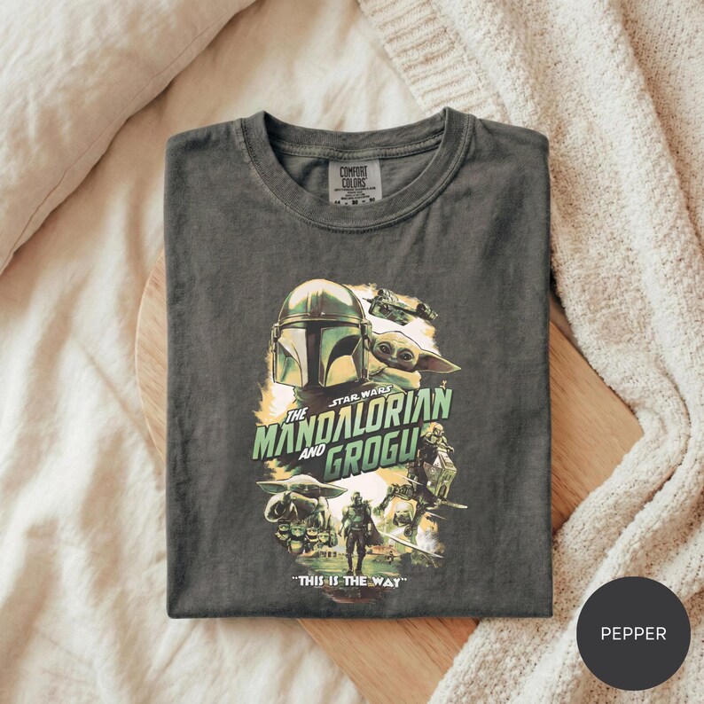 A t-shirt with a graphic design featuring characters from the Star Wars series, specifically The Mandalorian and the Frogs.