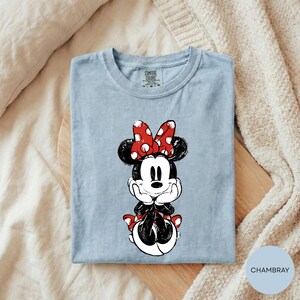 A light blue t-shirt with a Minnie Mouse graphic printed on it, placed on a wooden surface.