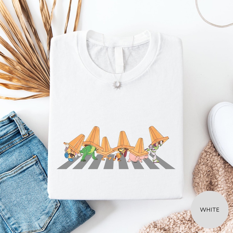 a white t-shirt with a graphic design of cartoon characters wearing orange hats, standing on a crosswalk.
