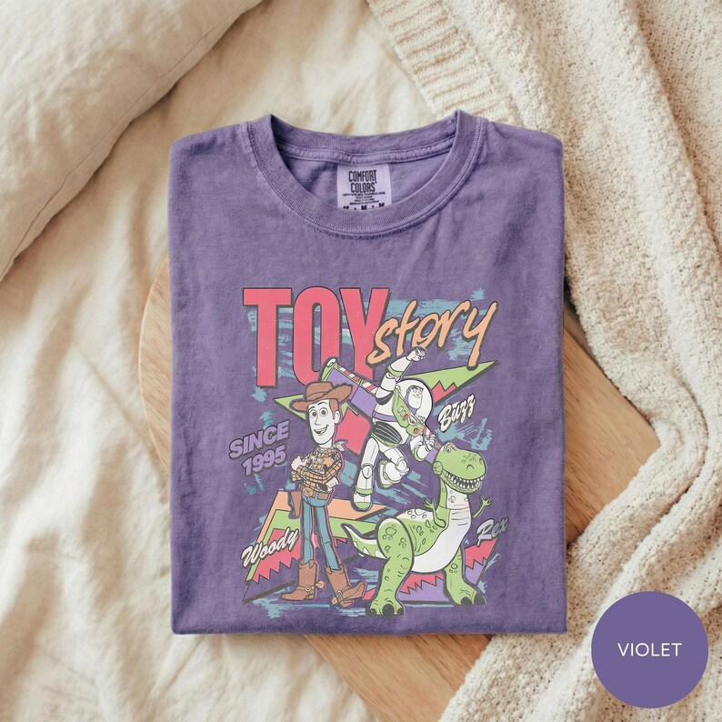 A purple t-shirt with a colorful graphic design featuring characters from the Toy Story movie, including Woody and Buzz Lightyear, along with the text "TOY STORY" and "SINCE 1995".