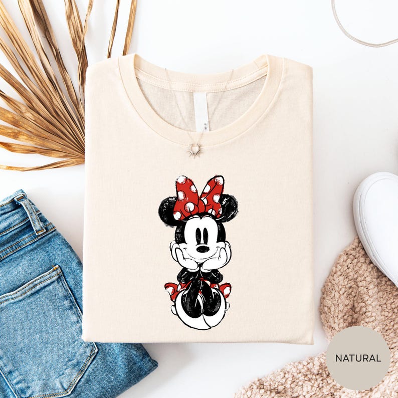 a white t-shirt with a Minnie Mouse graphic printed on it, along with a pair of blue jeans and a beige sweater.