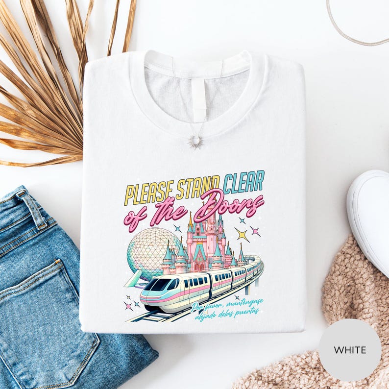 a white t-shirt with a colorful graphic design depicting a train and a castle, along with the text "Please stand clear of the doors".