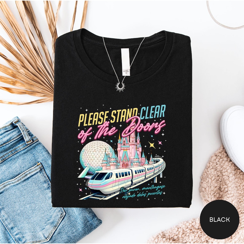 a black t-shirt with a colorful graphic design depicting a train and a castle, along with the text "Please stand clear of the doors" and "The doors are closing".