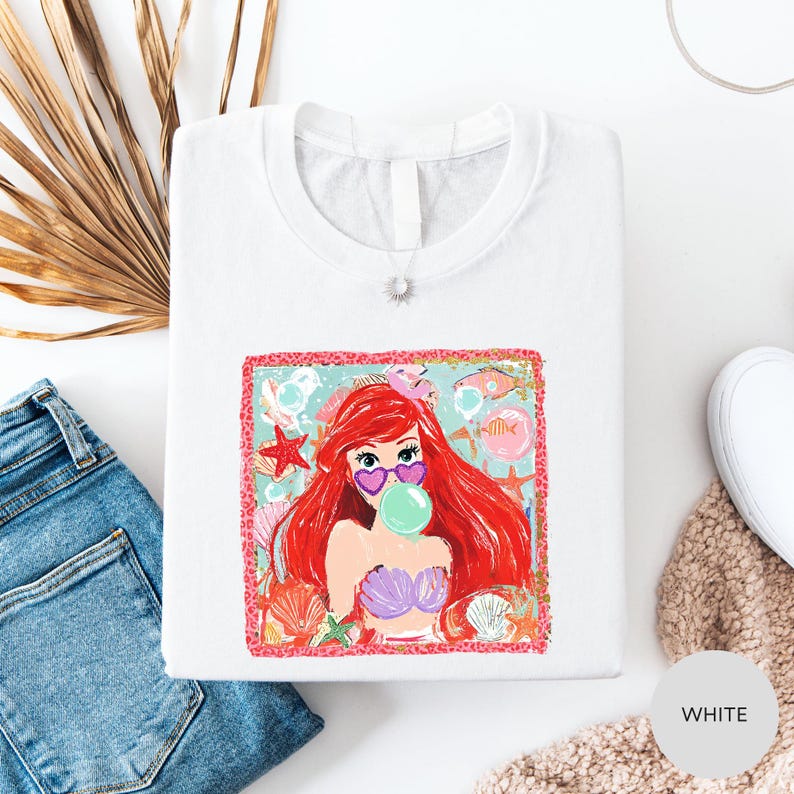 a white t-shirt with a colorful graphic of a mermaid character, along with a pair of blue jeans and some other clothing items.