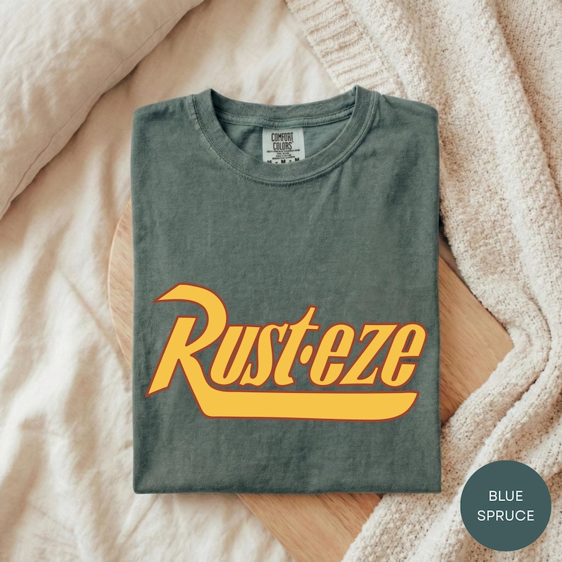 a gray t-shirt with the word "Rusteze" printed on it, laid out on a wooden surface.
