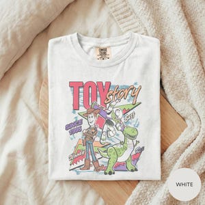 A white t-shirt with a colorful graphic design featuring characters from the Toy Story movie, including Woody and Buzz Lightyear.