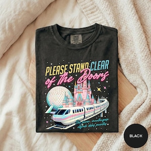 A black t-shirt with a colorful graphic design depicting a train and a castle, along with the text "Please Stand Clear of the Doors" and "Disneyland" written on it.